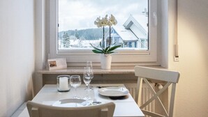 Une table à manger ornée d’un vase de fleurs blanches, d’un calendrier et de verres à vin.