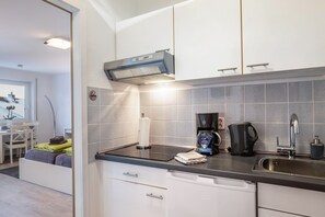 Une cuisine moderne avec un plan de travail noir, des placards blancs, une machine à café et une bouilloire.