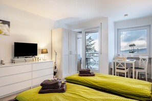 Habitación de hotel moderna con dos camas, televisor, escritorio y sillas, y vistas al exterior.
