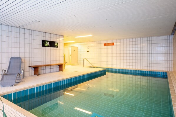 An indoor swimming pool with tiled walls, a bench, and a chair. - Studio 'Schwarzwaldblick D with Pool' with Mountain View and Wi-Fi (Schönwald im Schwarzwald)