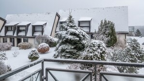 A residential building with multiple roof levels, snow-covered trees, and a fenced balcony area. - Studio 'Schwarzwaldblick F with Pool App 3' with Balcony and Wi-Fi (Schönwald im Schwarzwald)