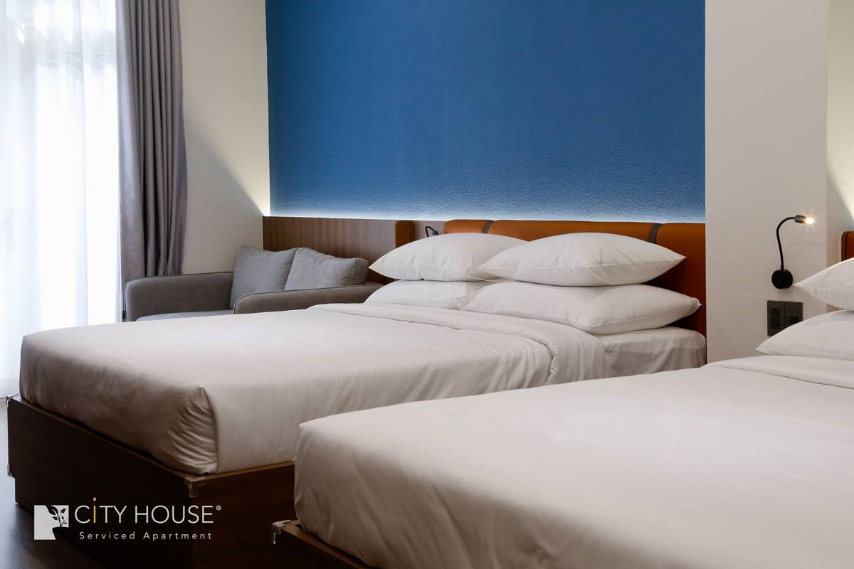 A hotel room with two beds, a sofa, and a large blue accent wall.
