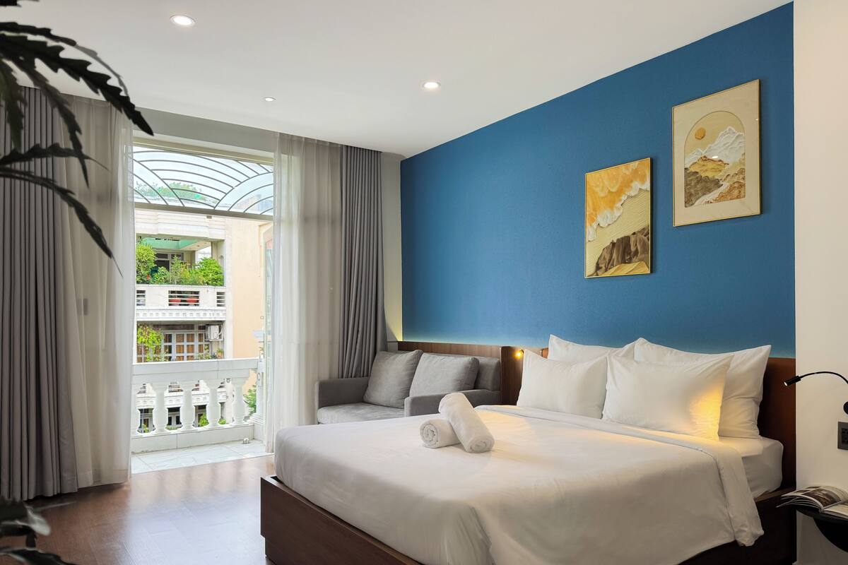 A hotel room with a large bed, a view of a balcony, and two paintings on the wall.