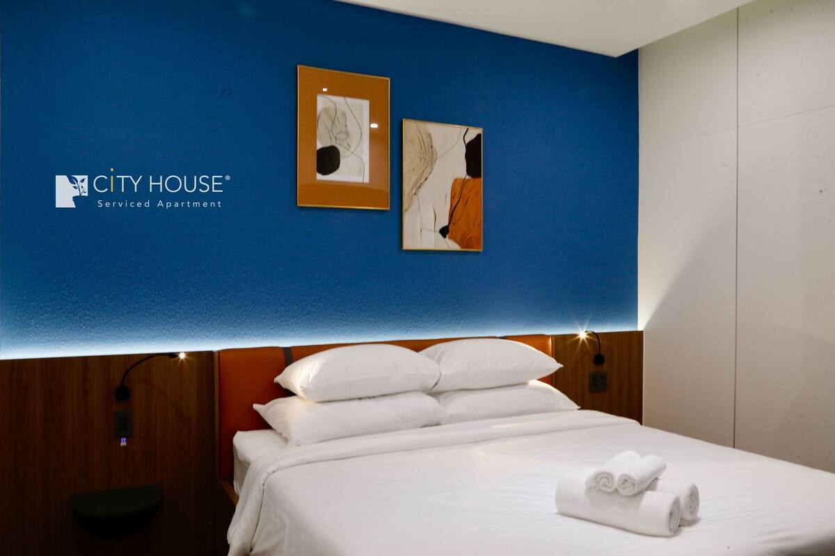 A hotel room with a bed, white pillows, and a blue wall with two framed artworks.