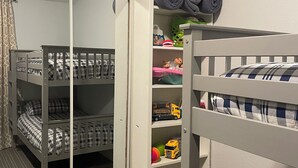 A child's room with a bunk bed, a wardrobe with a mirror, and shelves with toys and folded clothes.