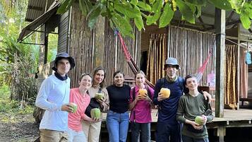 A group of people standing in front of a rustic wooden structure with a thatched roof, surrounded by trees.
