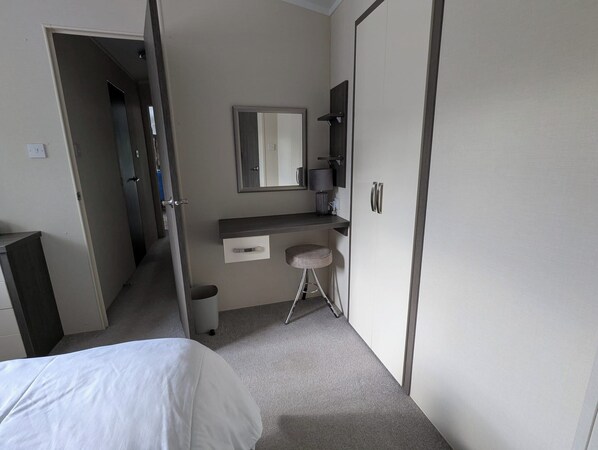 A bedroom with a bed, a small desk with a chair, a mirror, and a wardrobe. - 2-Bed Ringwood Cabin - incl Park Pass, SelfCheckin (Ringwood)
