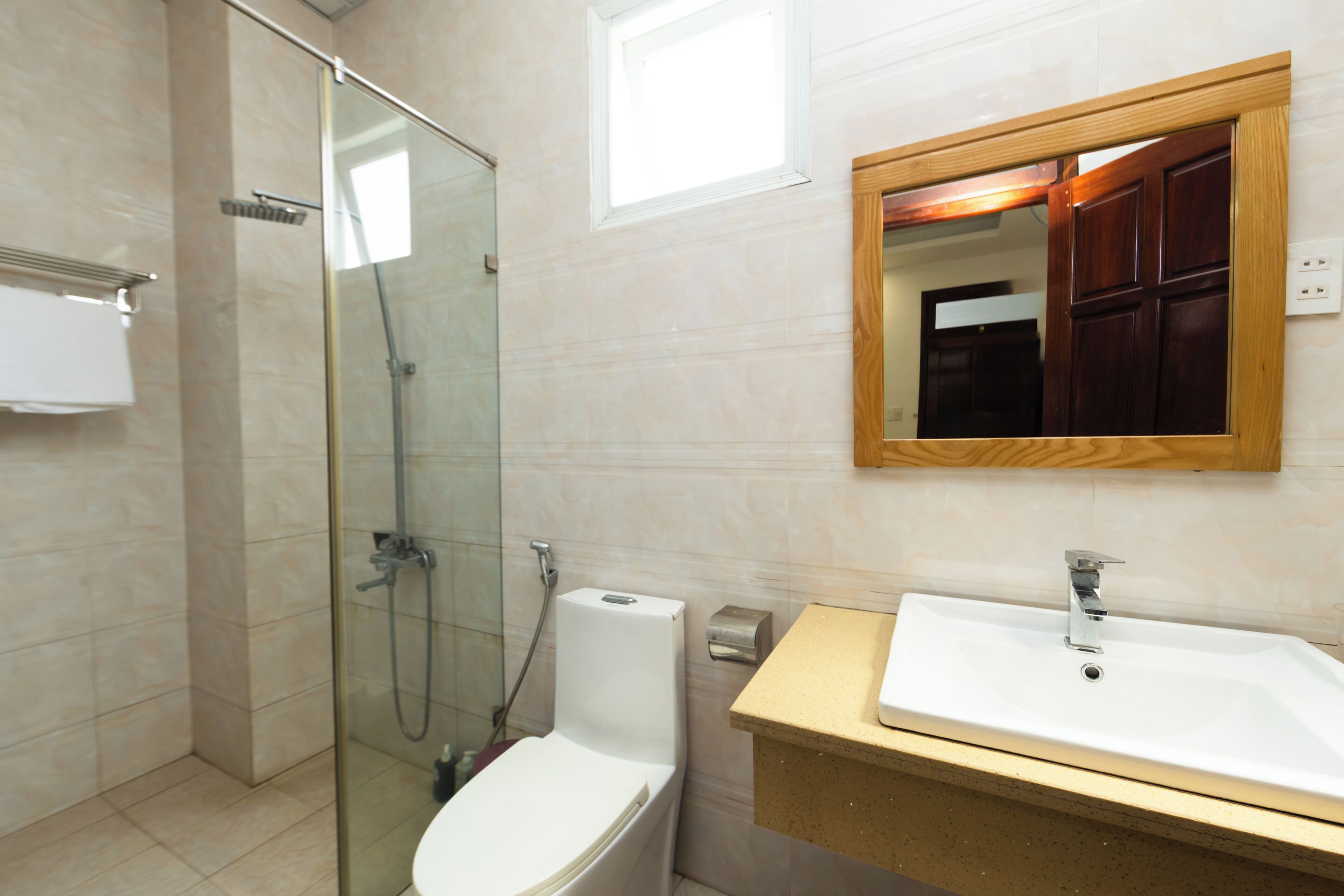 A modern bathroom with a glass shower enclosure, a white toilet, a sink with a wooden countertop, and a mirror with a wooden frame.