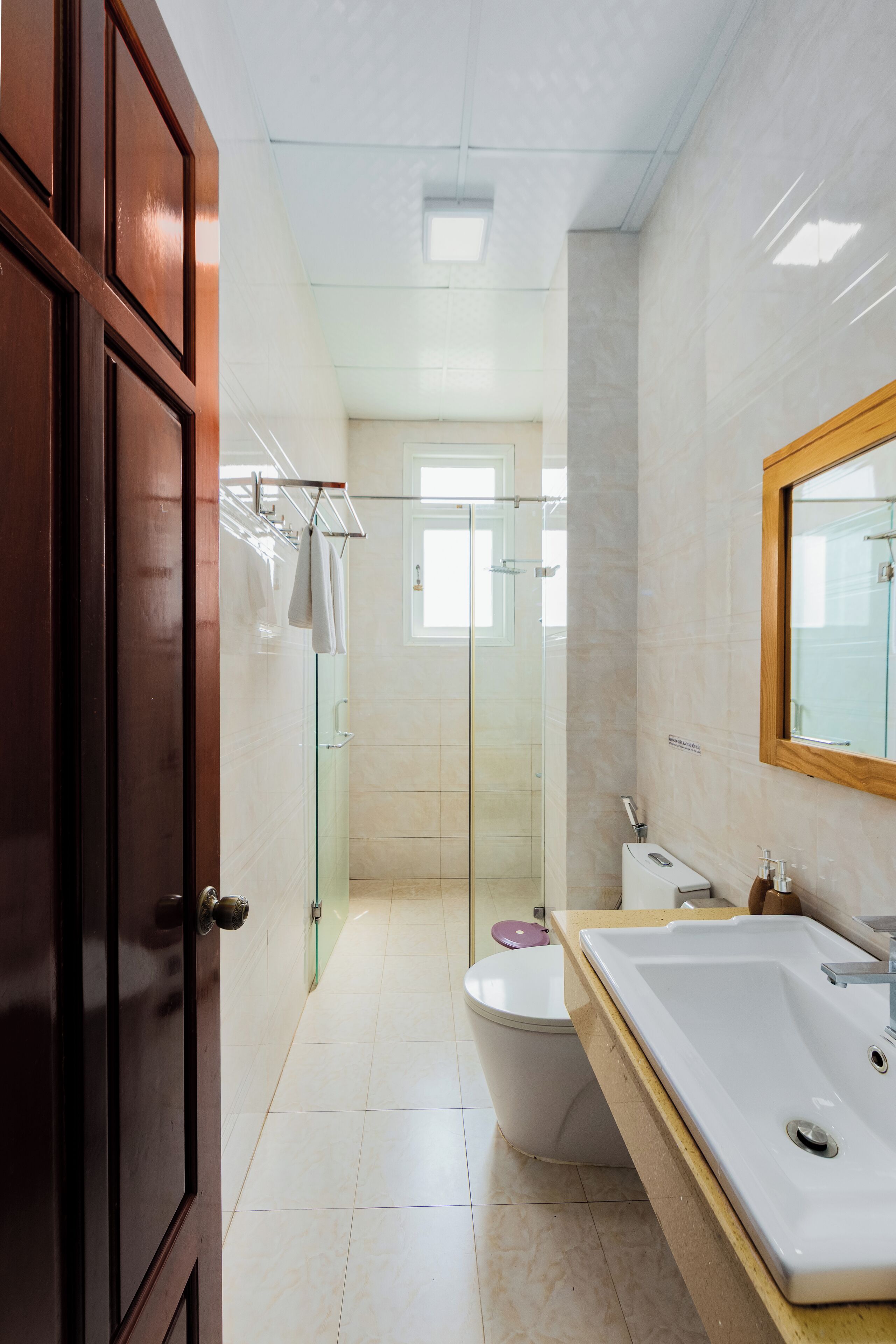 A modern bathroom with a glass shower enclosure, a white sink, and a wooden door.