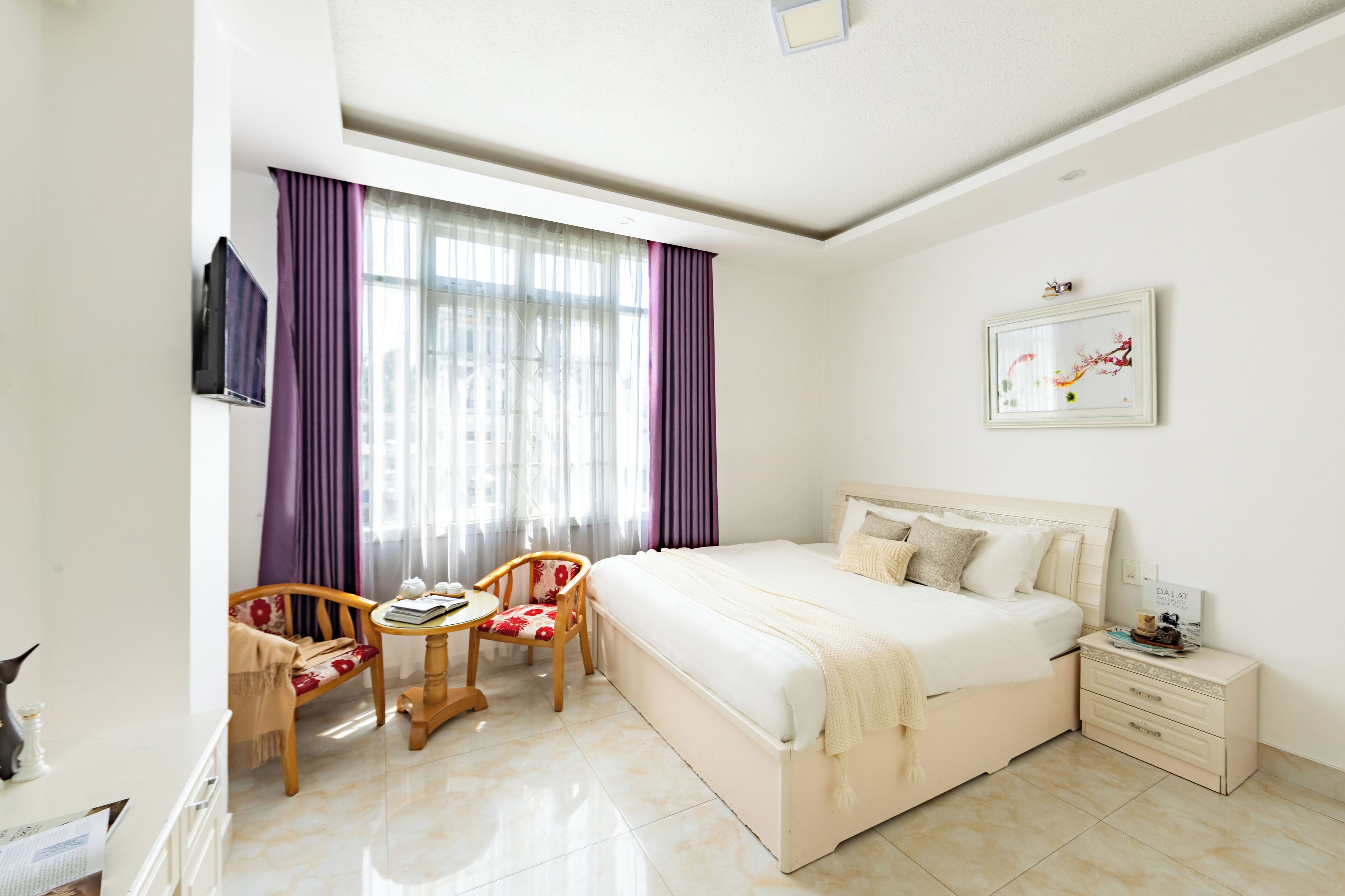 Une chambre d’hôtel avec un lit, une chaise, une petite table, un téléviseur et une table de chevet.