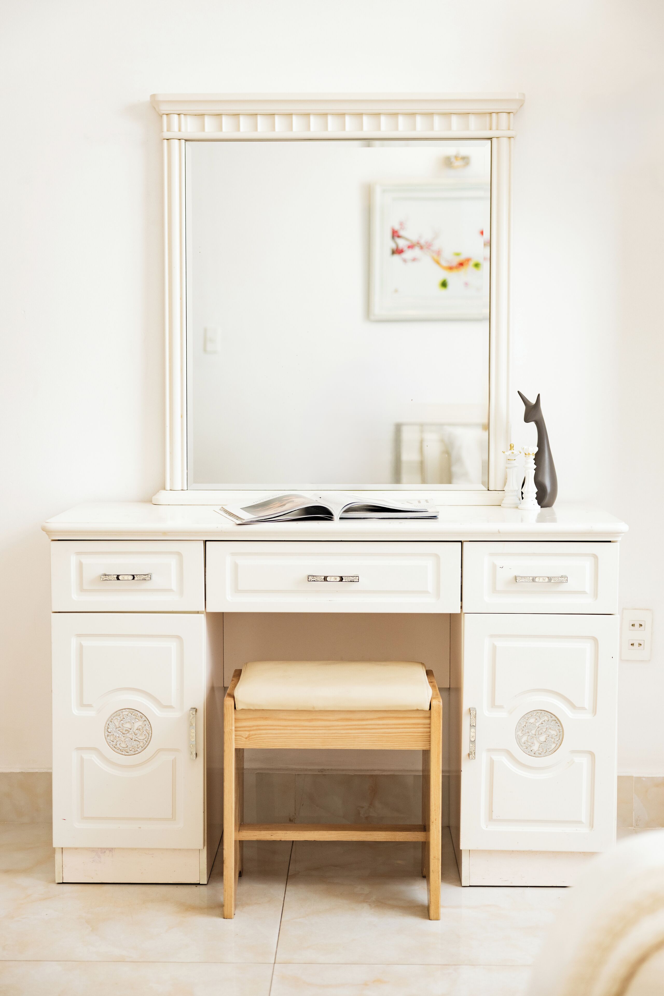 A white vanity with a mirror, a small stool, and a decorative cat statue.