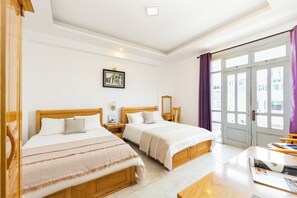 Ein Hotelzimmer mit zwei Holzbetten, einem großen Fenster mit Vorhängen, einem Holztisch und einem gerahmten Bild an der Wand.