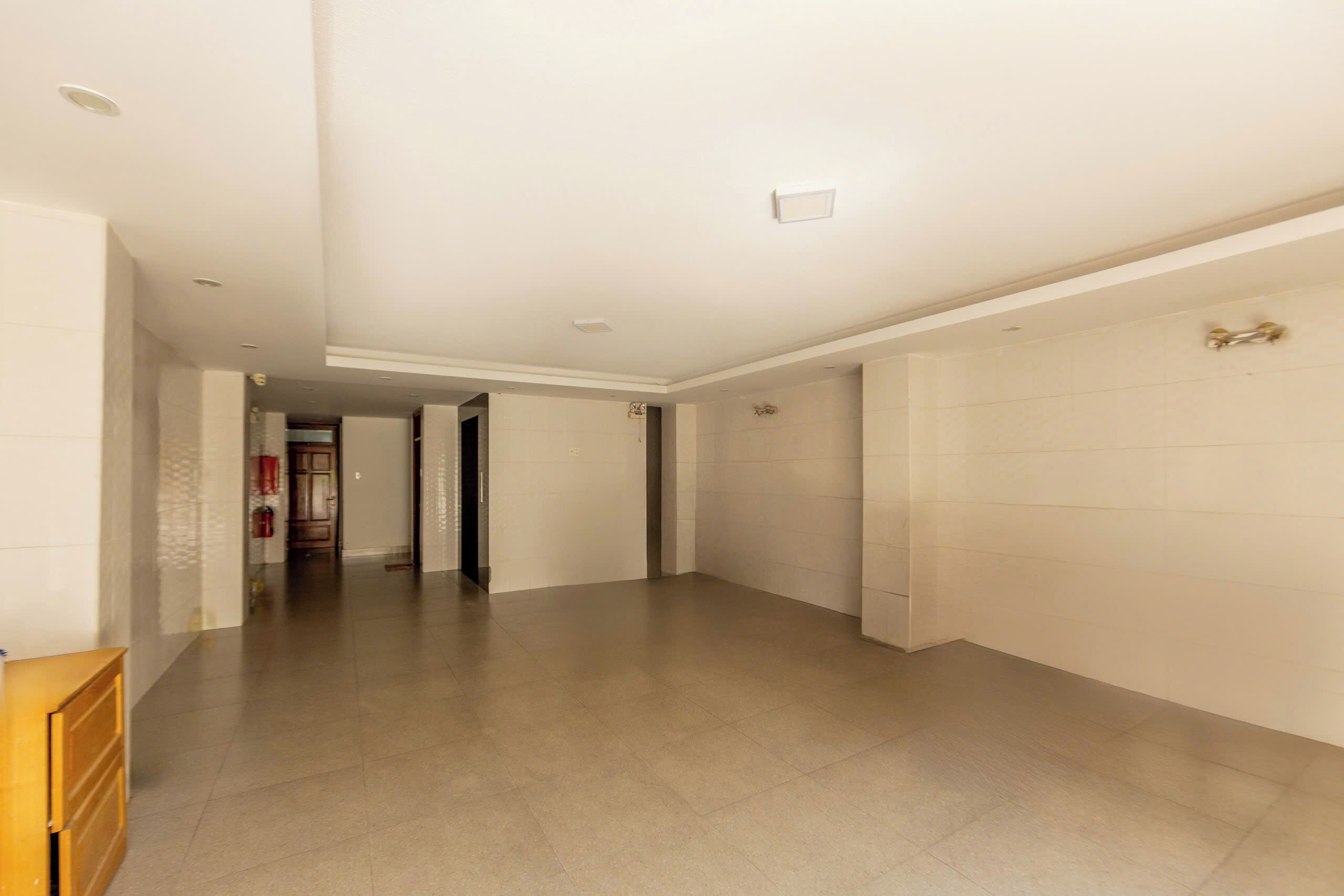 A spacious hallway with a tiled floor and white walls, leading to a door at the end.