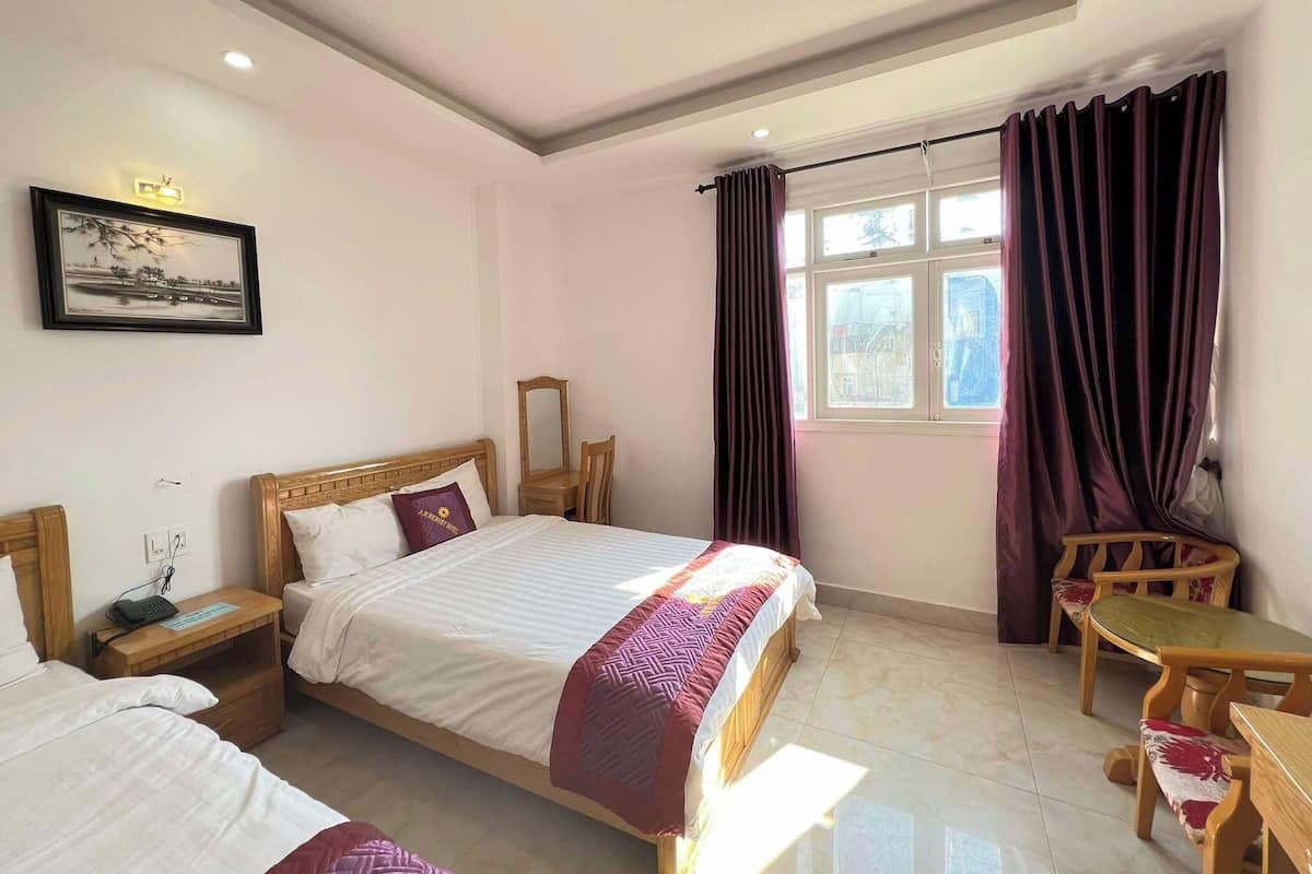 Habitación de hotel con cama, mesita de noche, silla y una pequeña mesa con otra silla.