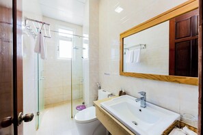 Ein Badezimmer mit Duschkabine aus Glas, einer weißen Toilette, einem Waschbecken mit Spiegel und einem Holzkabinet.