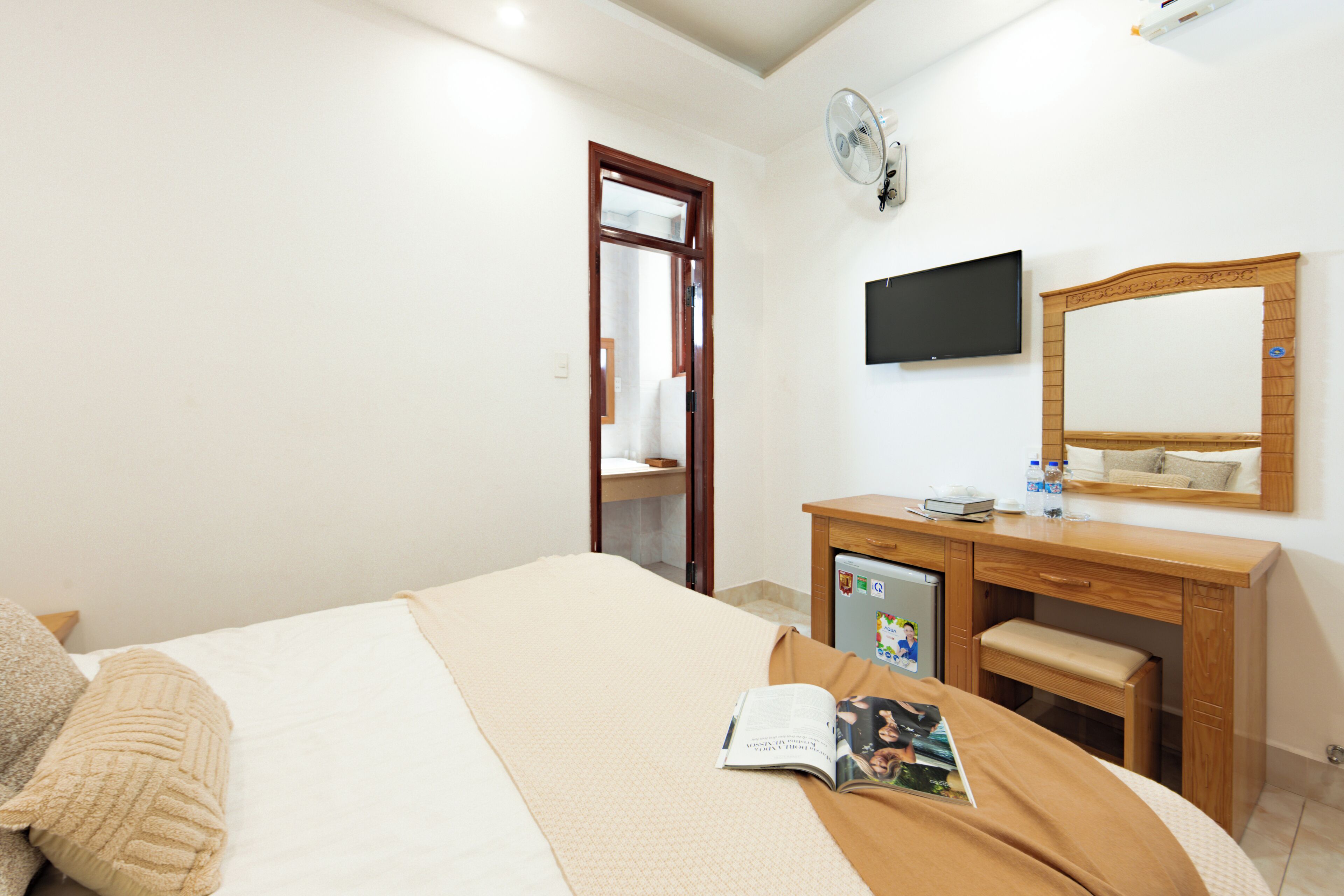 Habitación de hotel con cama, un escritorio de madera con espejo, televisor y un refrigerador pequeño.