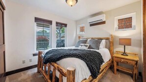 A bedroom with a wooden bed, a bedside table with a lamp, a window with blinds, and an air conditioning unit on the wall. - Pet Friendly Dover Bay Getaway (Dover)