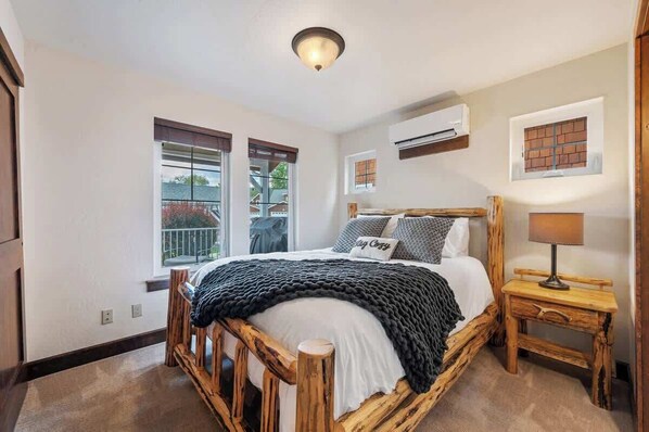 Een slaapkamer met een houten bed, een nachtkastje met een lamp, een raam met zonwering en een airconditioning aan de muur.