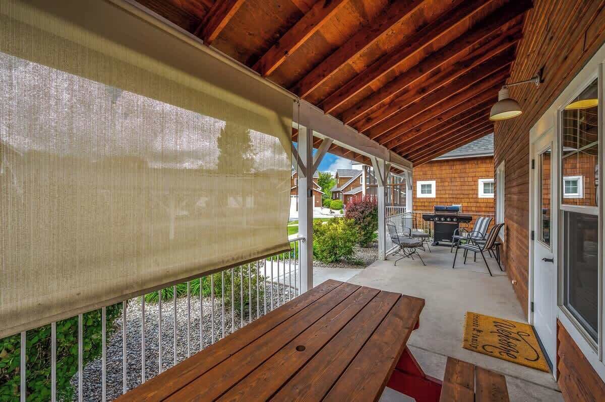 Une terrasse couverte avec une table et des chaises en bois, un barbecue et une vue sur les maisons voisines.