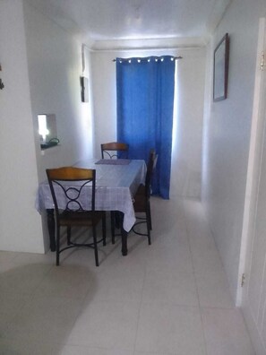 A dining area with a table set for four, a blue curtain, and a small shelf with a mirror.