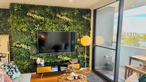 Un salon moderne avec un mur vert, un téléviseur à écran plat, une table basse en bois et un canapé.