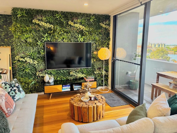 A modern living room with a green wall, a flat-screen TV, a wooden coffee table, and a sofa.