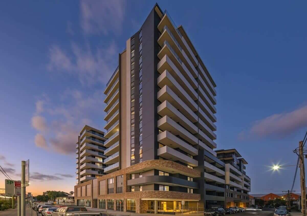 A high-rise hotel with multiple balconies, a central entrance, and a parking area.