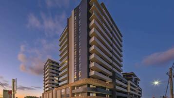 A high-rise hotel with multiple balconies, a central entrance, and a parking area.