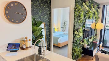 A modern hotel room with a kitchen area, a large mirror, and a green wall with plants.