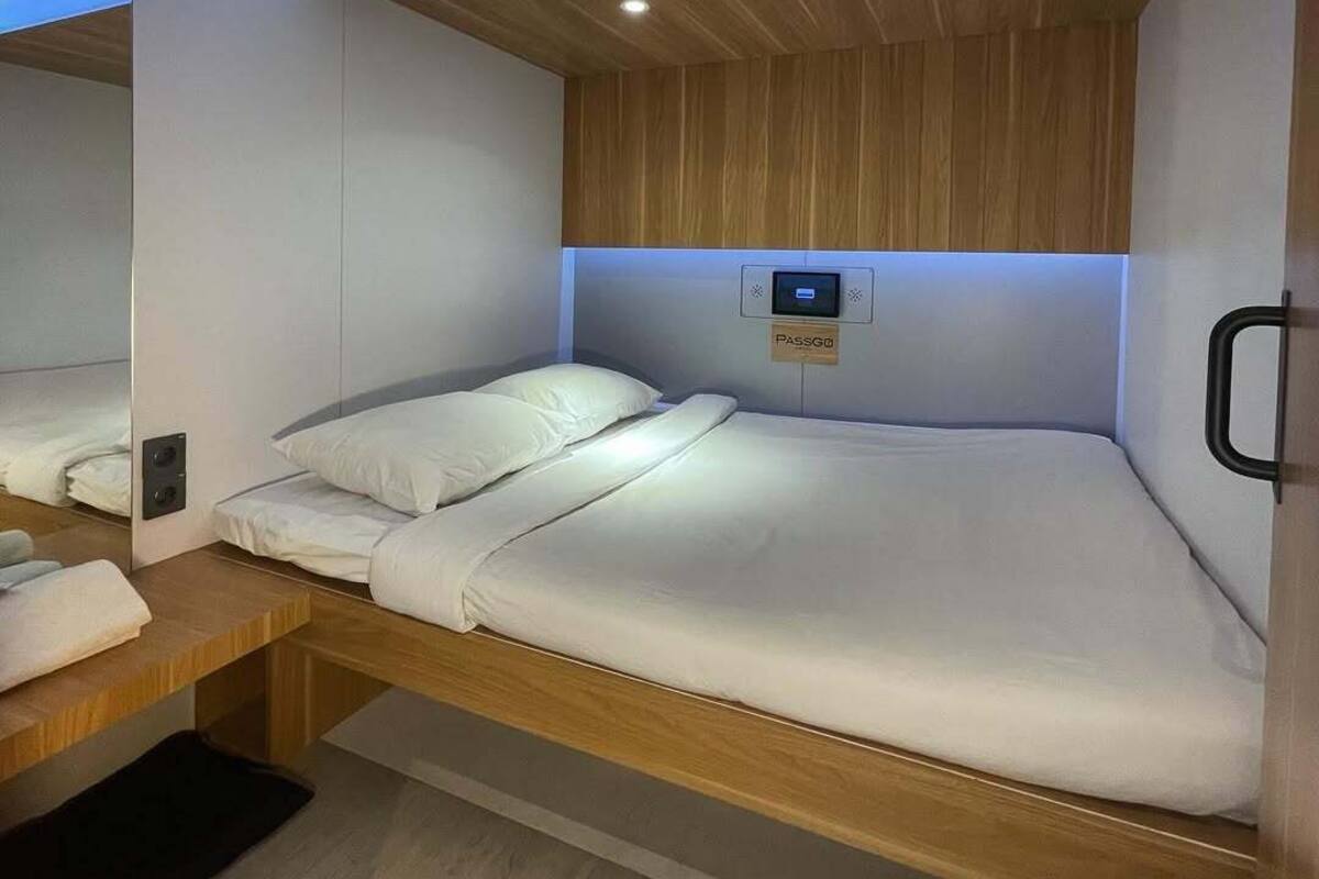 A modern, compact room with a bed, a control panel, and a mirror.