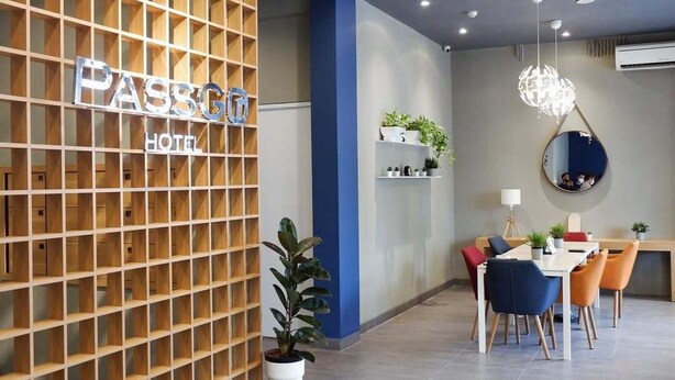 En moderne hotellobby med en væg af trælameller, en receptionsdisk, et spiseområde med stole og borde samt en hængende lysearmatur.