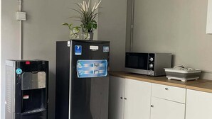 Et tekøkken med et sort køleskab, en vanddispenser, en mikrobølgeovn og en lille bordplade med en opvaskestativ.