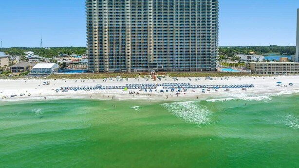 A high-rise hotel with a beach view, located near a sandy beach with umbrellas and lounge chairs.