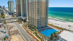 A high-rise hotel with a pool, beachfront view, and a busy street in the background.