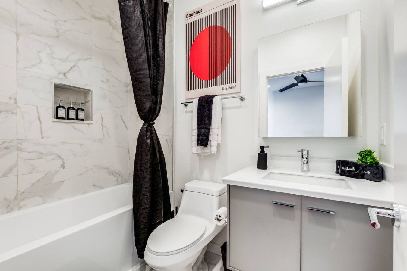 A modern bathroom with a white toilet, a black shower curtain, a white sink with a mirror above it, and a towel rack.