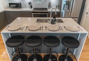 A modern kitchen with a central island, bar stools, and stainless steel appliances. - Dallas 2BR Retreat | Rooftop Patio & Stunning Downtown Skyline (Dallas)