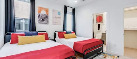 Une chambre d’hôtel avec deux lits, un ventilateur de plafond, des œuvres d’art accrochées aux murs et une salle de bain visible à travers une porte ouverte.