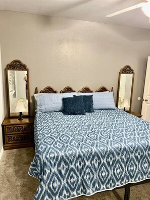 A bedroom with a patterned bedspread, two nightstands with lamps, and a ceiling fan.