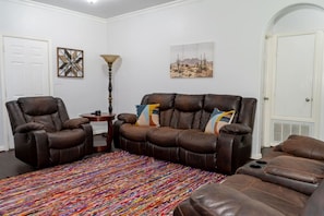 A living room with a brown leather sofa, a recliner, a colorful rug, and a lamp. - Corinth 3BR | BBQ Grill + Backyard & Playground (Corinth)
