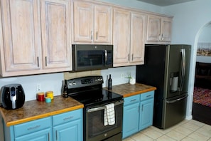 A kitchen with light wooden cabinets, a black microwave, a stainless steel refrigerator, a black stove, and a blue countertop.