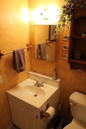 A bathroom with a sink, mirror, towel rack, and toilet. - Lighthouse-Themed Lake House Escape (Nocona)