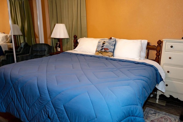 A hotel room with a large bed, a bedside table, a lamp, and a chair.