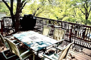 An outdoor patio with a table and chairs, surrounded by a wooden deck and trees.