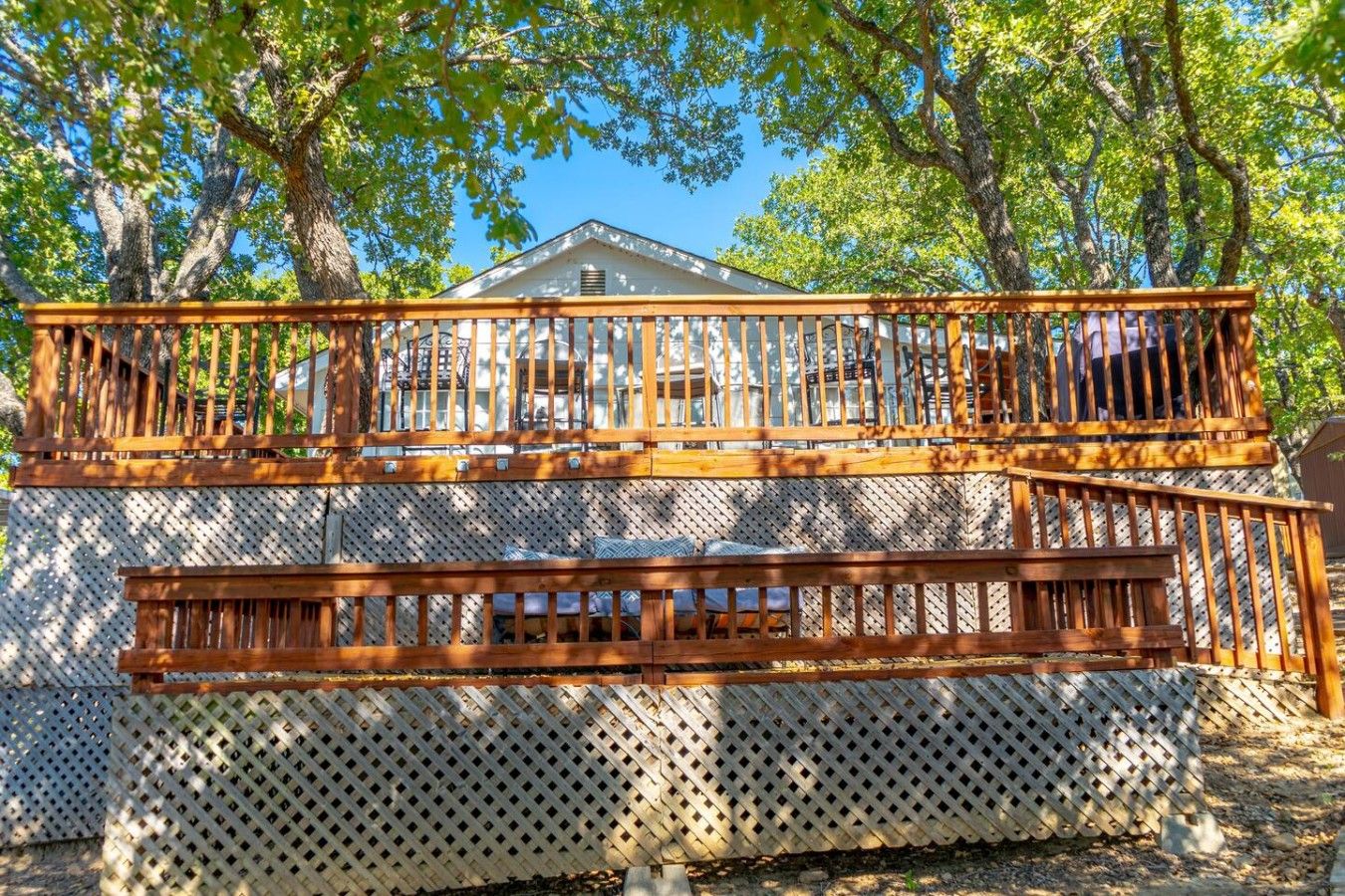 Una terraza de madera con un cerramiento de celosía y una casa al fondo.