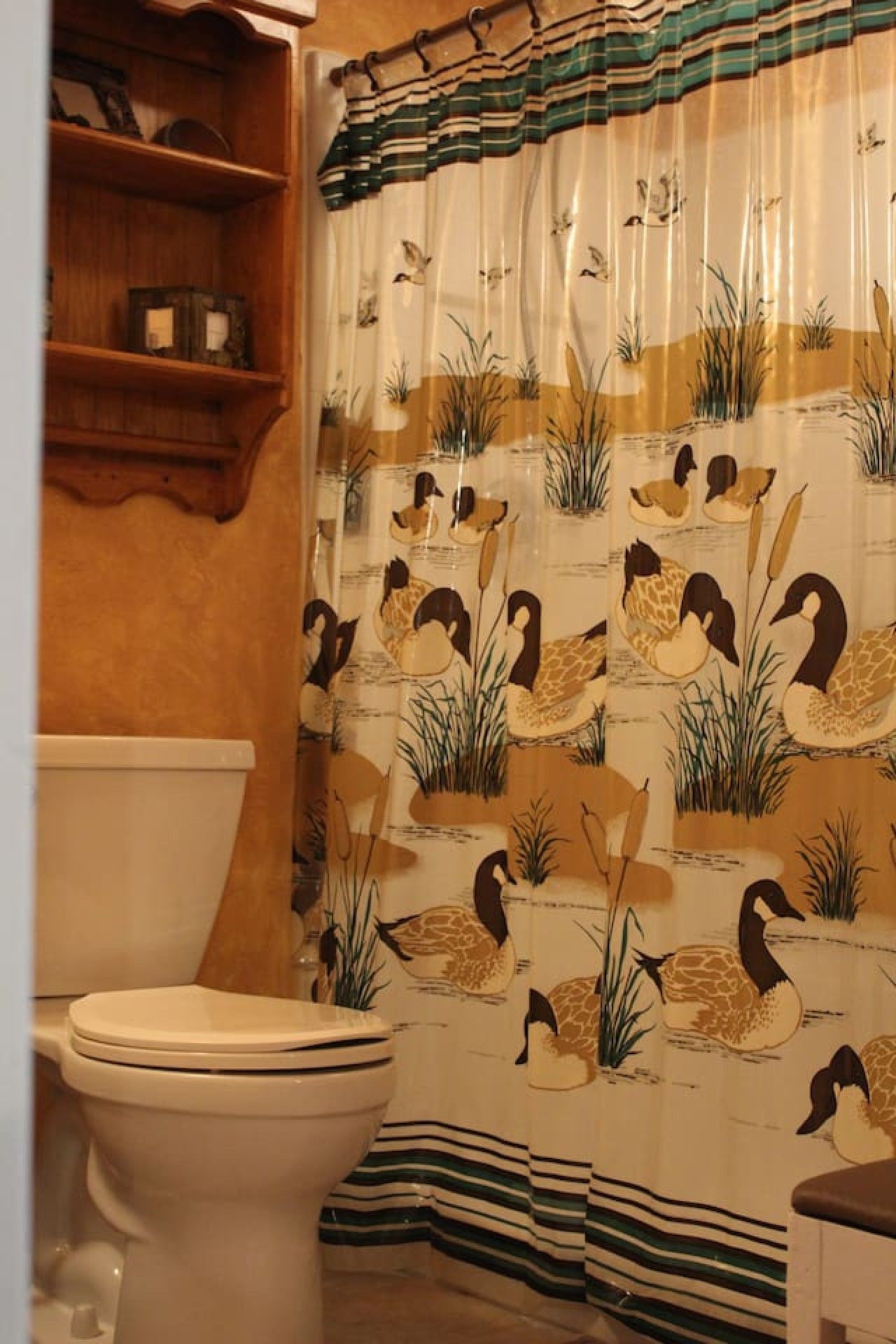 Un baño con inodoro, estantes de madera y cortina de ducha con estampado de patos.