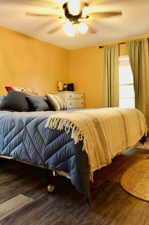 A bedroom with a bed, a nightstand, a ceiling fan, and a window with curtains.