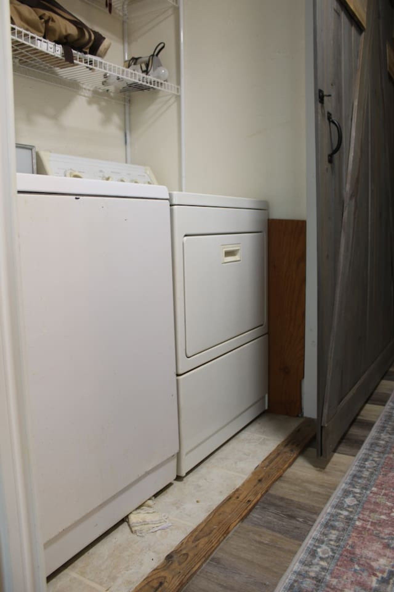 Une buanderie équipée d’un lave-linge et d’un sèche-linge, d’une étagère où sont rangés divers objets, et d’une porte en bois.