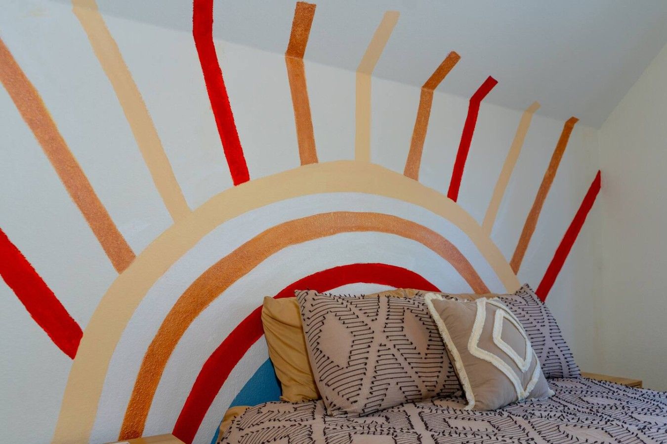 A bedroom with a bed, pillows, and a wall with a sun-like pattern.