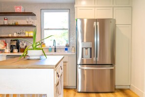 A modern kitchen with a stainless steel refrigerator, a wooden countertop, and a window providing natural light. - 3BR Saint Jo Getaway | BBQ, Fire Pit + Comfort (Saint Jo)