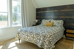 A bedroom with a bed, a nightstand, a lamp, and a view of the outdoors.
